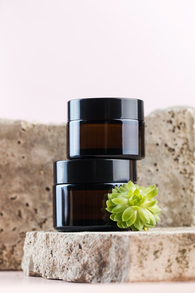 Jars with natural cosmetic products and succulents on concrete plates on pink